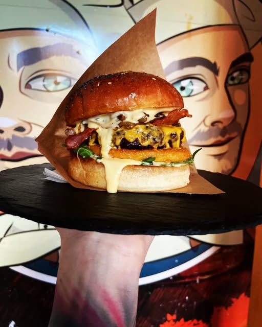 Burger so syrom, slaninou a cibuľkou pred nástennou maľbou U Bronďaka